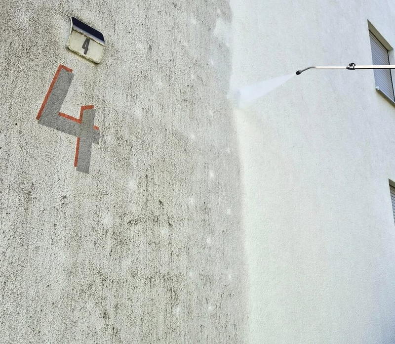 Nahaufnahme des Wasserstrahls an der Fassade, scharfe Kante zwischen verschmutztem und gereinigtem Putz