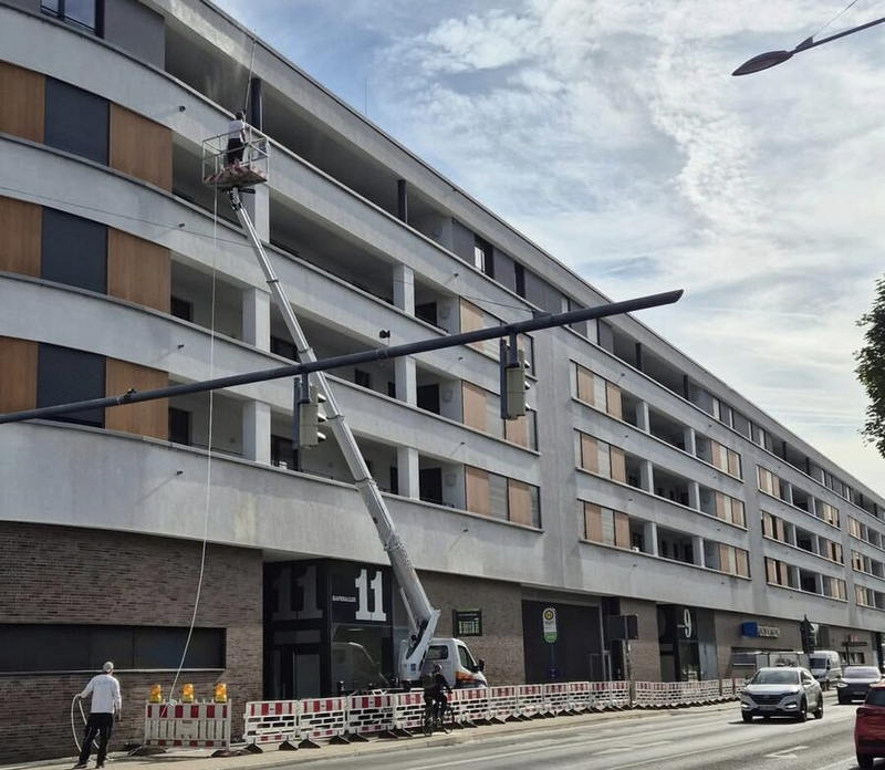 Hebebühne vor einem großen Wohn- und Geschäftskomplex während der Fassadenreinigung